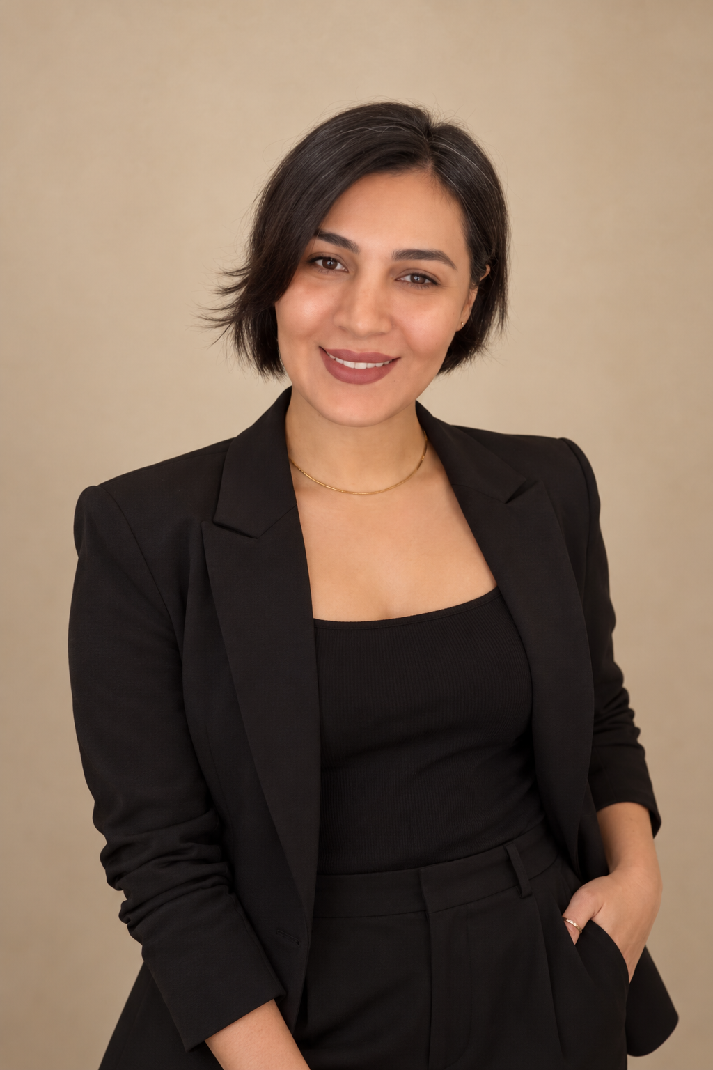 Frame Lash beauty professional with a dark bob hairstyle wearing a black blazer against a warm beige studio background.