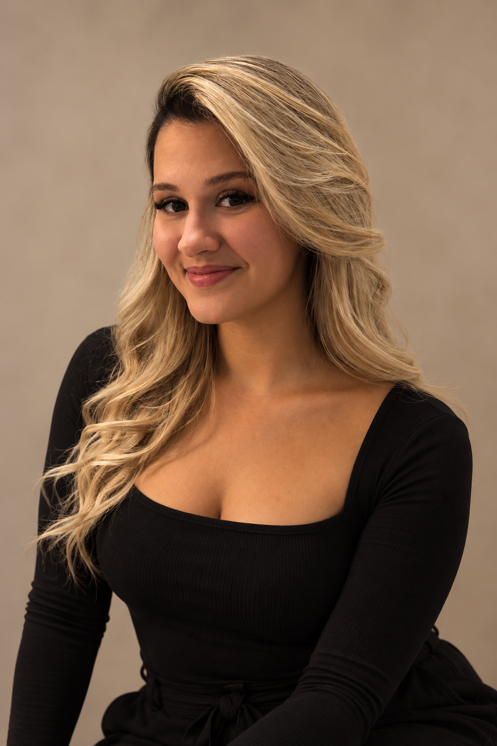 Frame Lash lash artist with long blonde hair wearing a black outfit against a warm beige studio background.