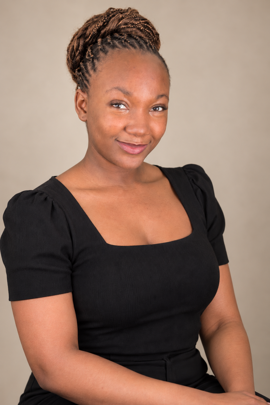 Professional staff portrait of a smiling woman with braided hair in a high bun, wearing a black square-neck top against a warm beige background.