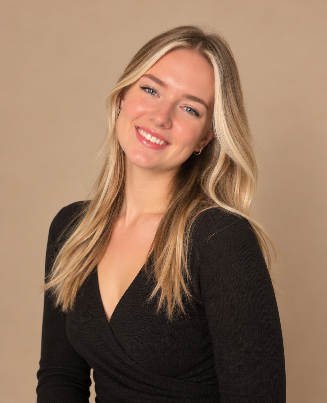 Blonde lash artist at Frame Lash wearing black against a warm beige studio background.