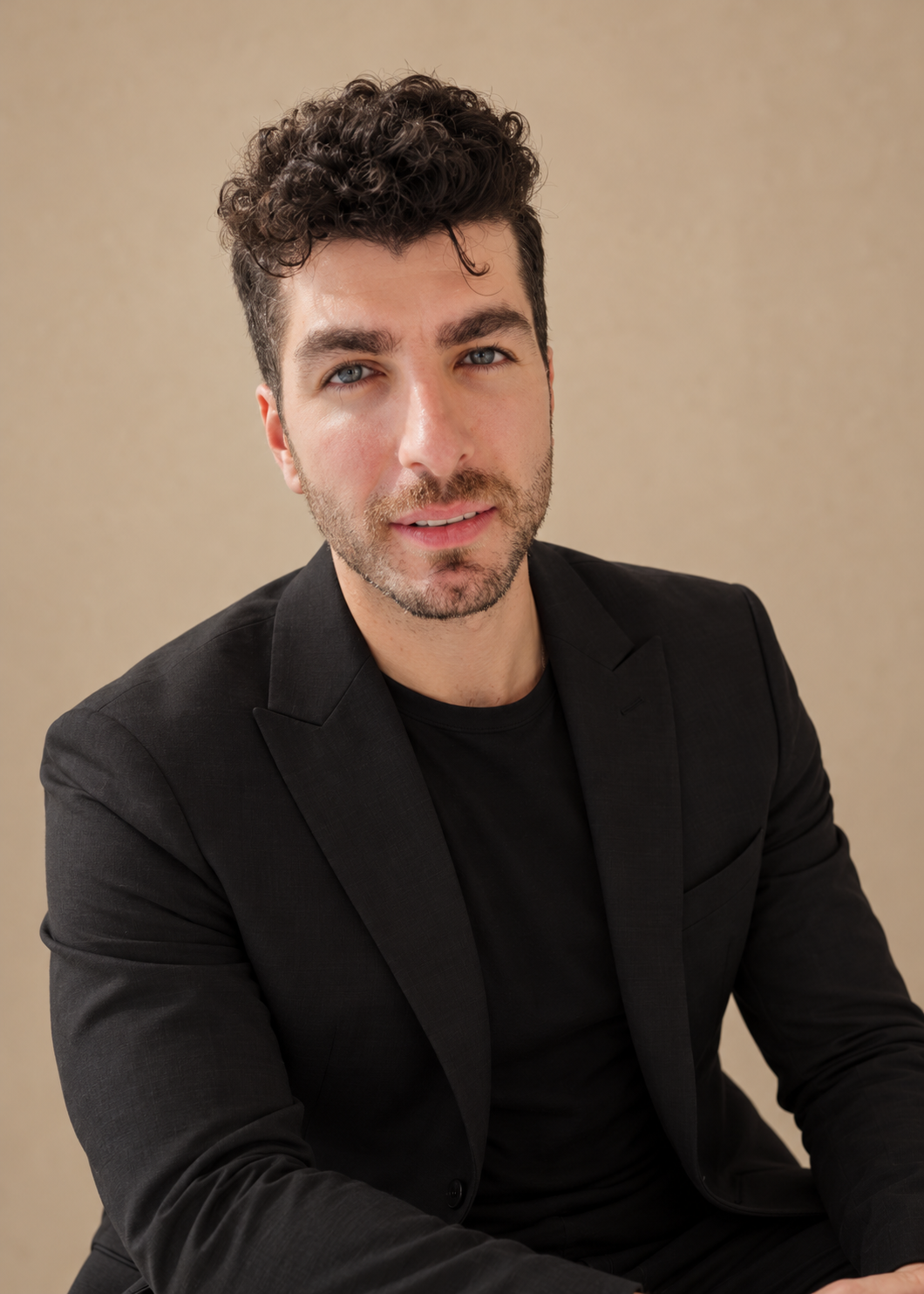 Frame Lash Studio team member with dark curly hair wearing an all-black outfit against a warm beige studio background.
