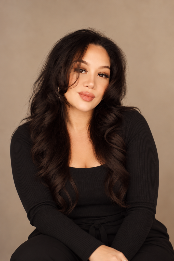 Frame Lash lash artist with long dark hair wearing a black outfit against a warm neutral studio background.